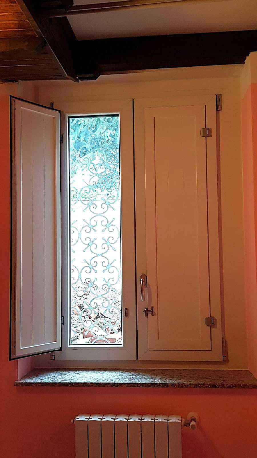 Finestra con inferriata decorativa e cassonetto in legno, in ambiente domestico.