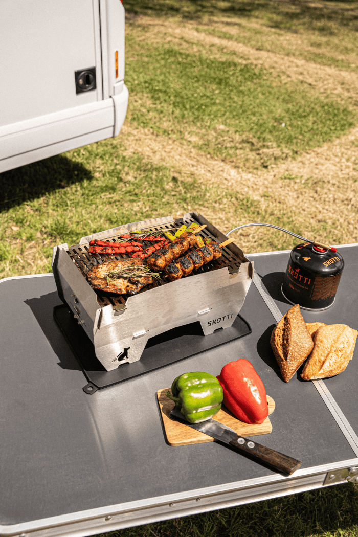 Skotti Matt portable grill cooking mixed meats and vegetables outdoors.