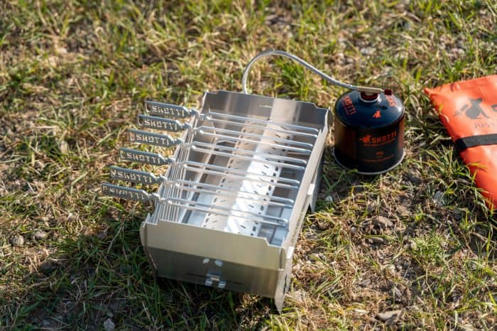 Portable Skotti Pikes camping stove with multiple burners on grassy terrain.