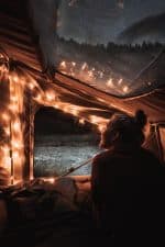 Woman relaxing inside a tent under starry night sky with string lights.