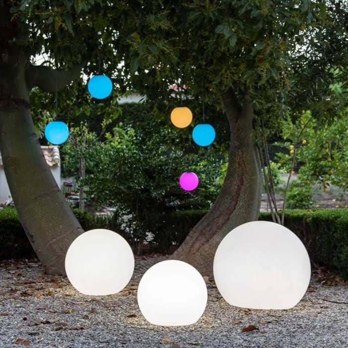Colorful solar-powered lanterns hanging from trees in outdoor setting.