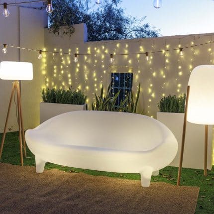 Modern white sofa with outdoor string lights and greenery backdrop.