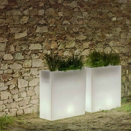 Modern solar-powered planters with lush green plants against a stone wall.
