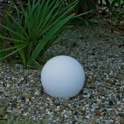 Floating solar light on pebble ground with greenery background.