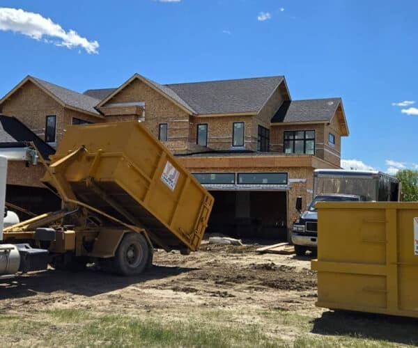 Dump truck collecting debris at a residential construction site for junk removal.