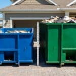 Blue and green dumpsters filled with trash outside a suburban home, ready for waste collection.