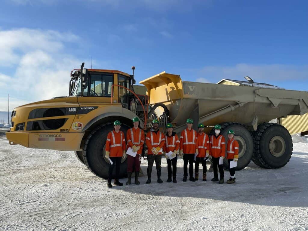 Heavy-duty mining truck with young workers in safety gear at resource industry site.