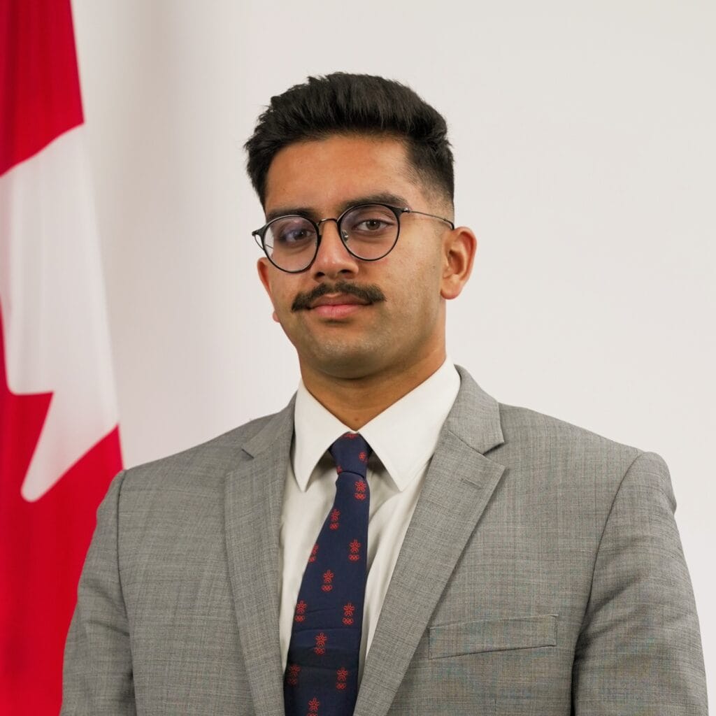 Young Canadian man in professional gray suit with Canadian flag in background.
