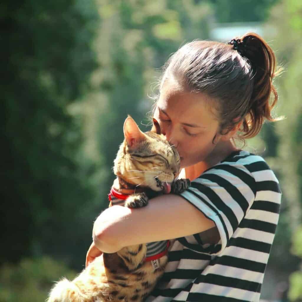 Young woman hugging and kissing a tiger cub outdoors in nature, promoting wildlife conservation and resource awareness.