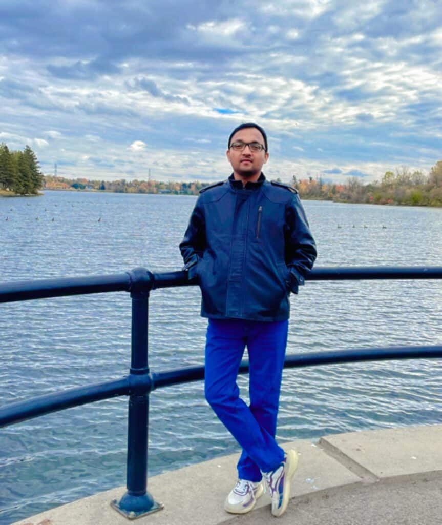 Young man standing by a lake with autumn foliage, representing Canadian resource sector advocacy.