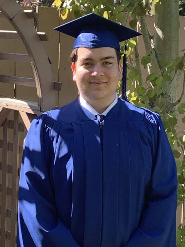 Young man in blue graduation gown and cap celebrating academic achievement outdoors.