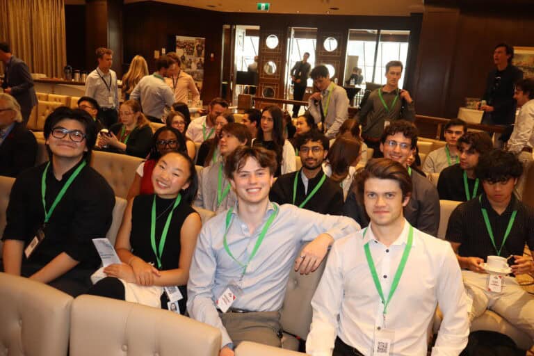 AI-generated group photo of young professionals attending a conference, featuring diverse individuals wearing ID badges in a warm, indoor setting filled with people, indicating a formal networking or seminar event.