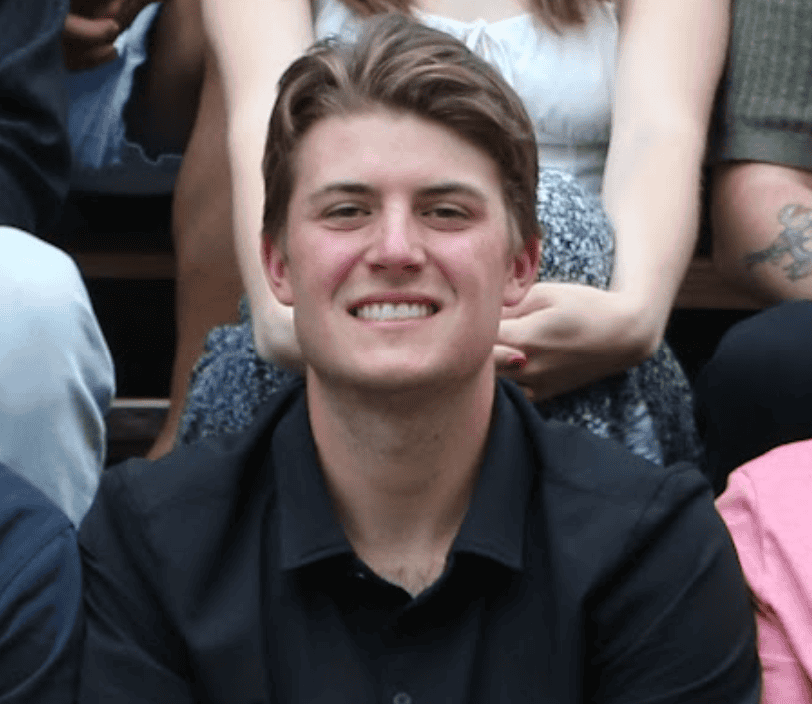 Young man smiling at an outdoor event with diverse friends.