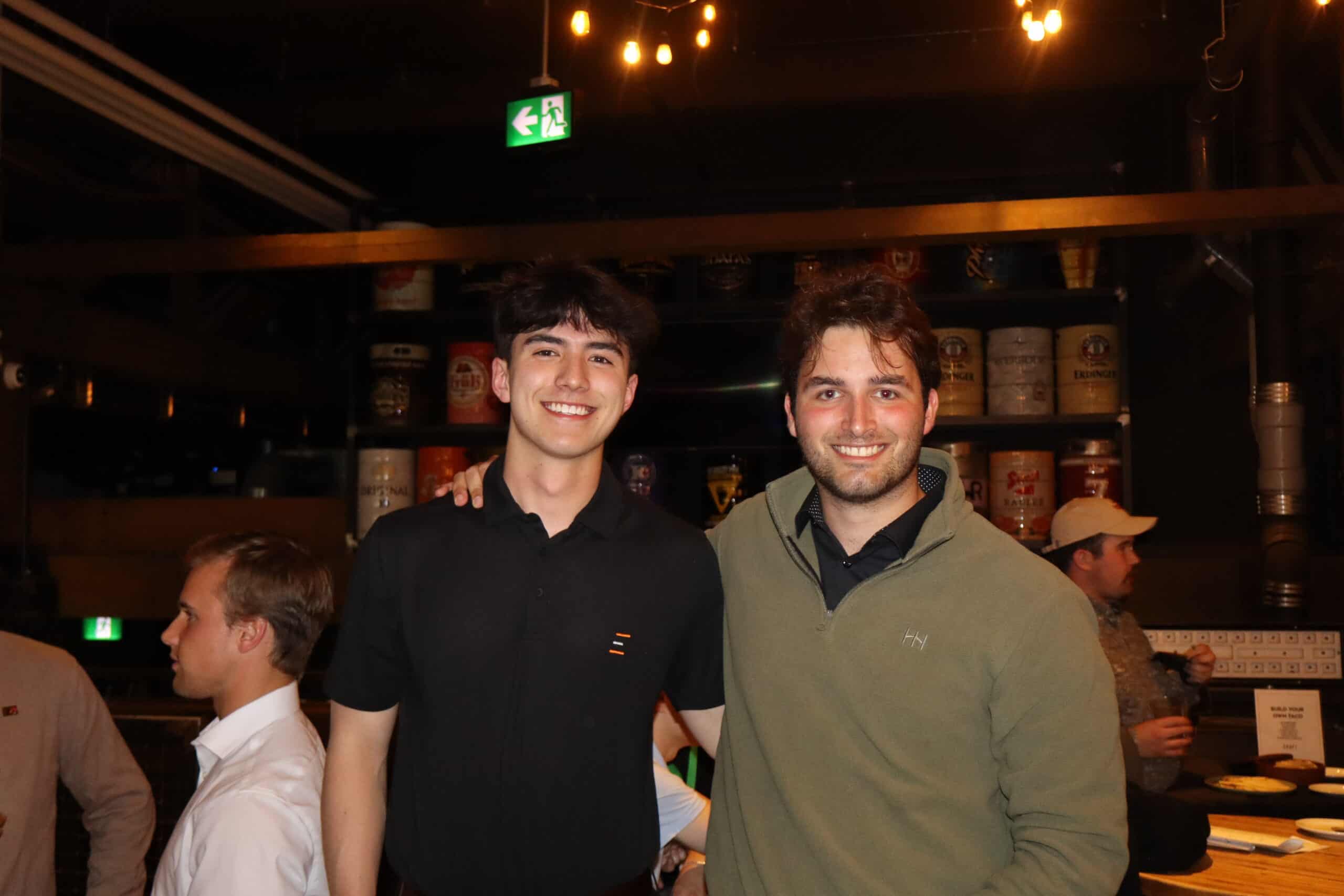 Two smiling men at a social event, representing innovative data center solutions in Alberta, with a lively background of industrial decor and ambient lighting.