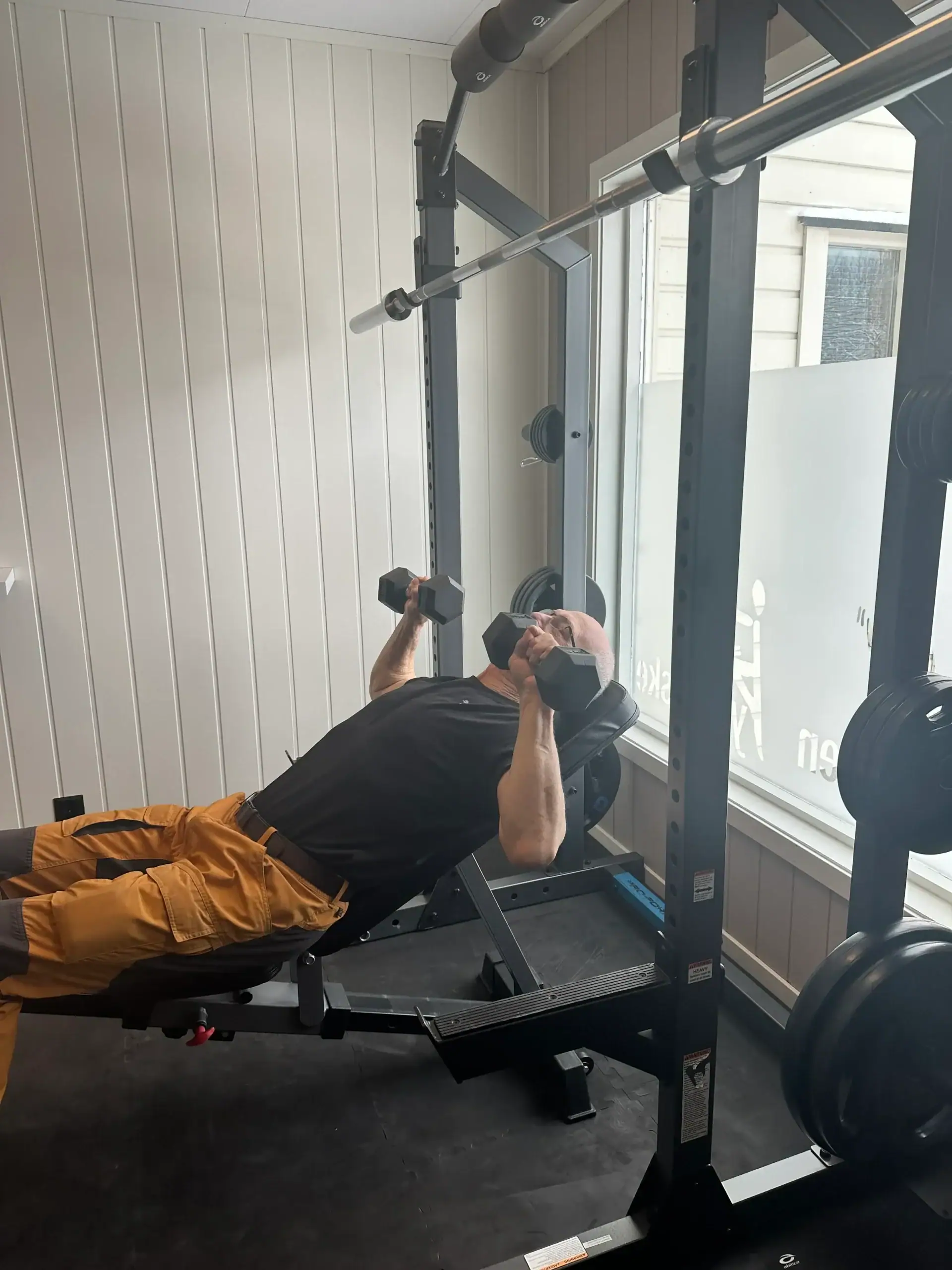 Mann trener med manualer i skrå benkpress som del av rehabilitering og styrketrening ved Ytteren Fysikalske i Mo i Rana.