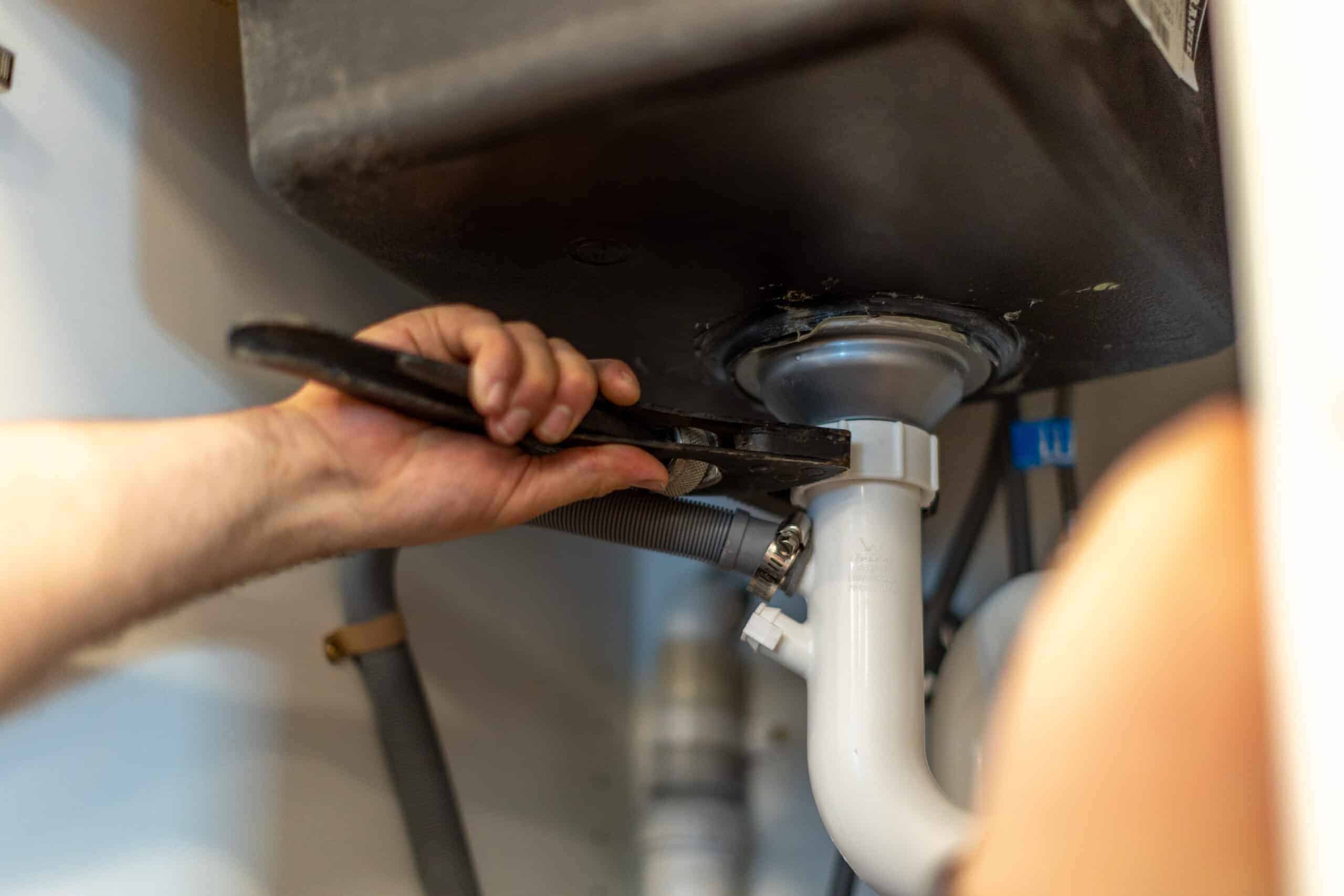 Technician fixing a blocked drain pipe under a sink in a kitchen.
