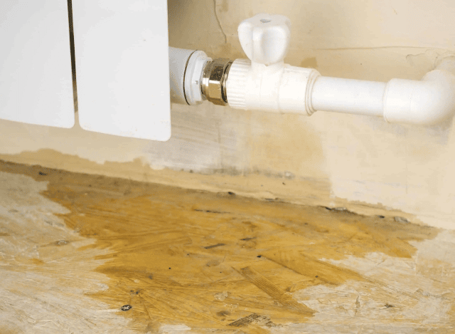Water leak under white pipe on wooden floor.