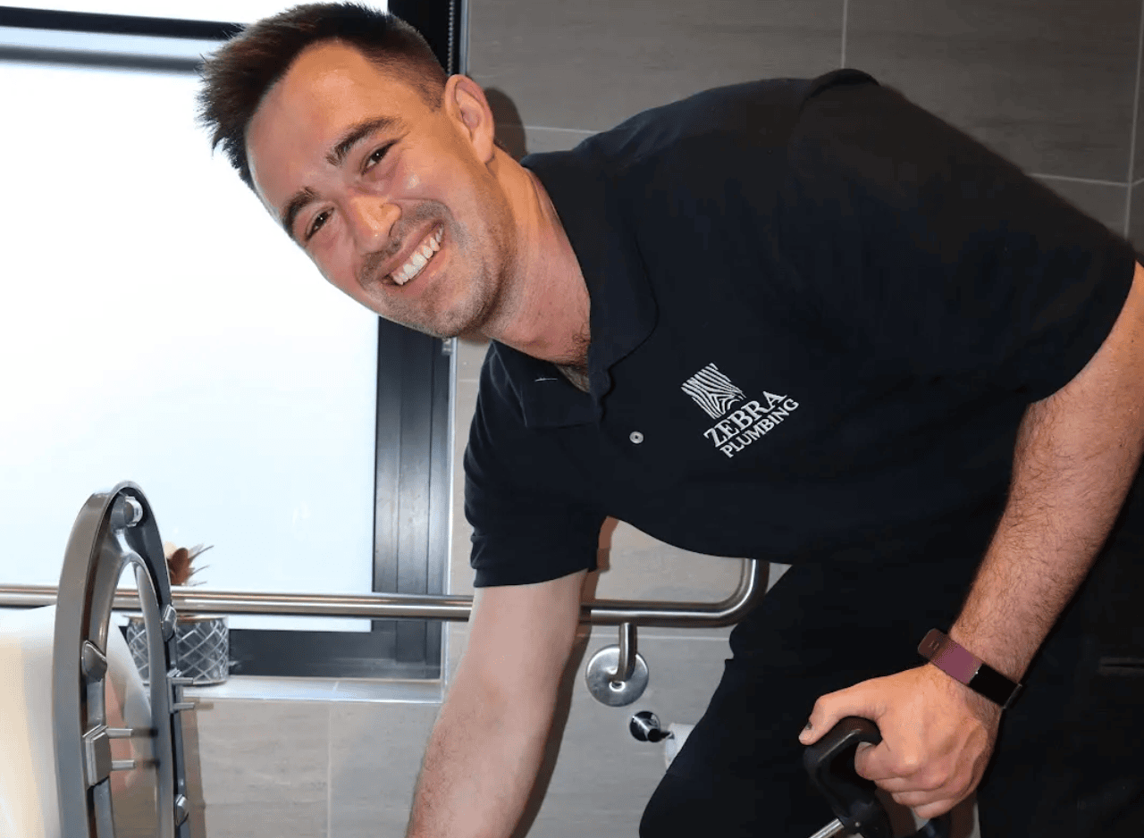 Plumber smiling while using a drain pump on a toilet.