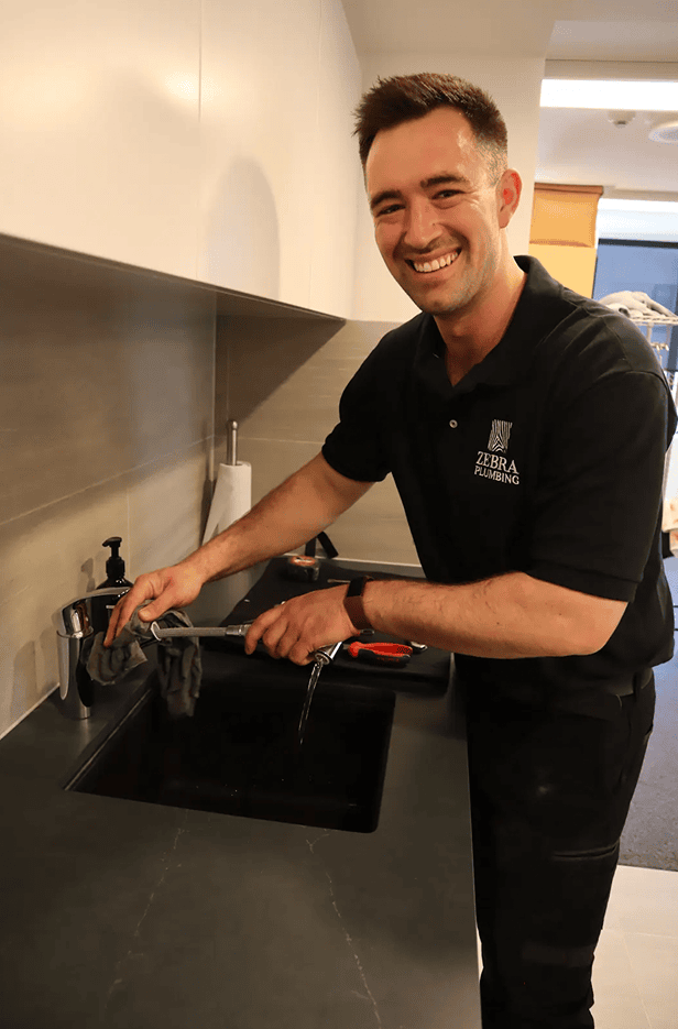 Zebra Plumbing technician smiling while testing a kitchen tap during a service call.