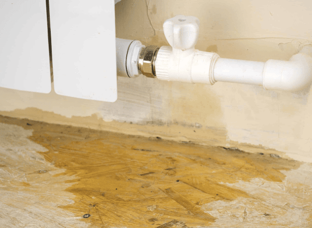 Water leak under white pipe on wooden floor.