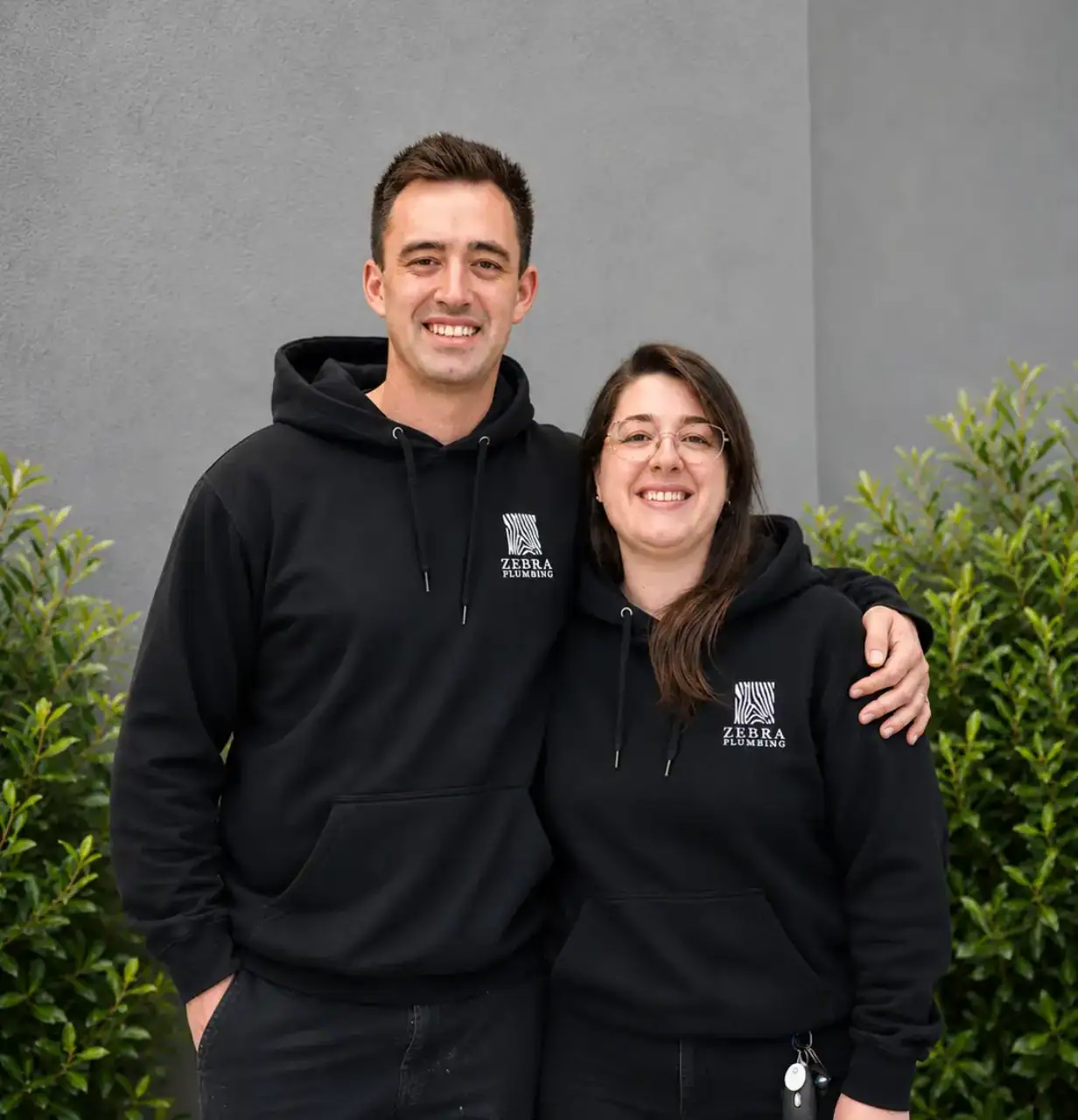 Zebra Plumbing team members in black hoodies smiling outdoors.