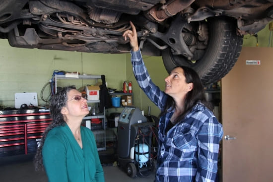 Auto repair technician inspecting vehicle underside for issues.