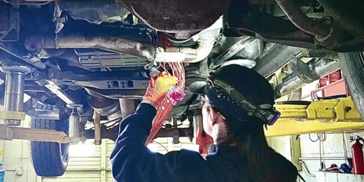 Automotive technician inspecting vehicle undercarriage for maintenance and repairs.