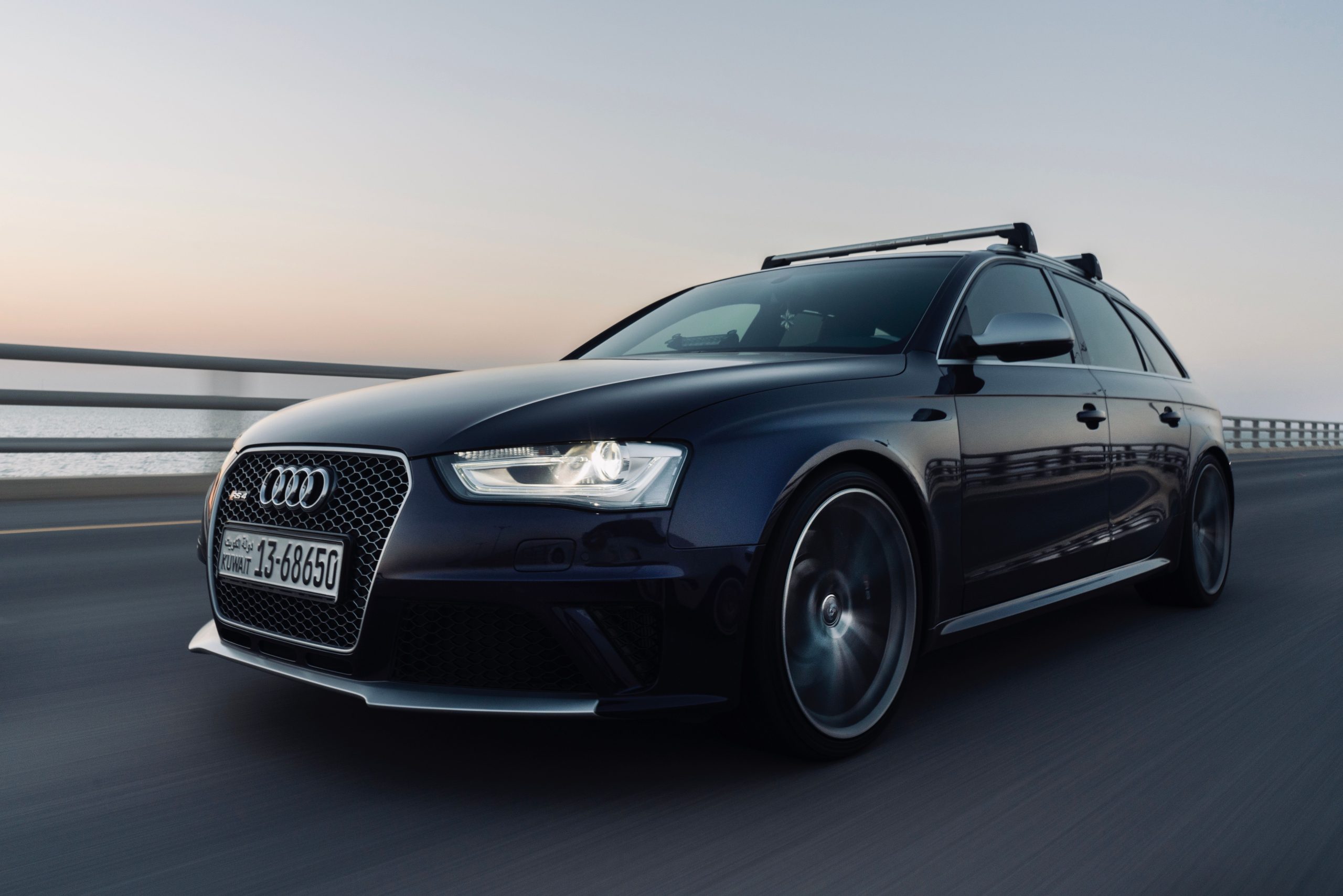 Black Audi station wagon driving on highway at sunset.