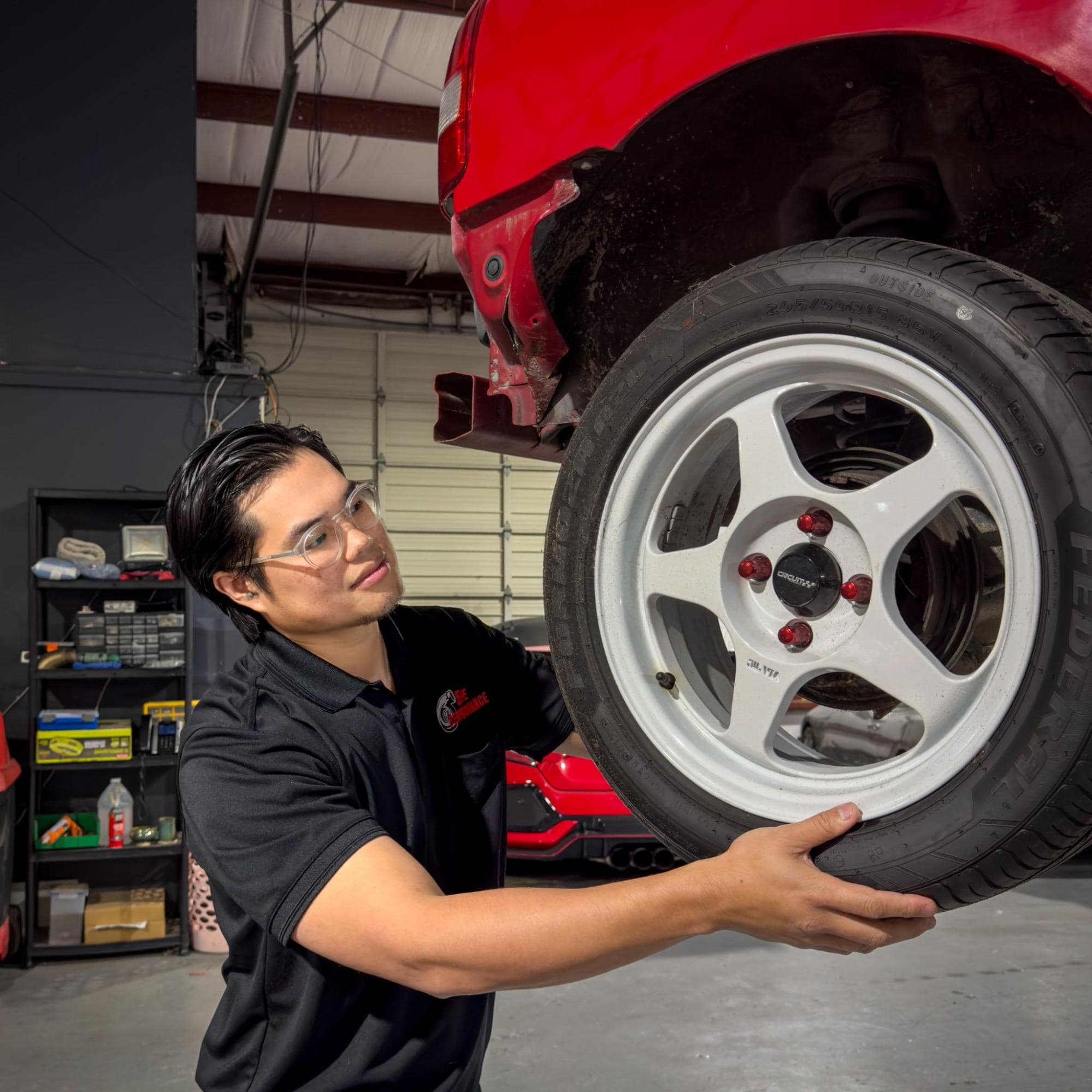 Technician inspecting a car tire at 5ive Performance auto shop.