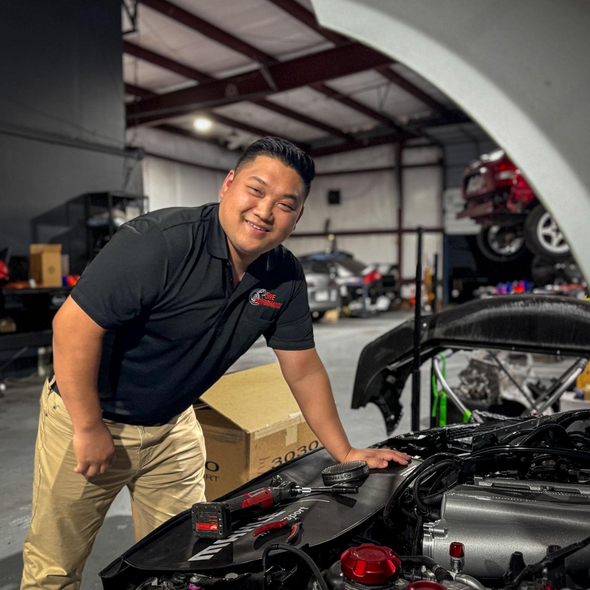 Automotive technician inspecting car engine at 5ive Performance auto shop.