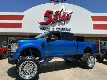 Lifted blue truck with oversized wheels at 5 Star Tires and Wheels.