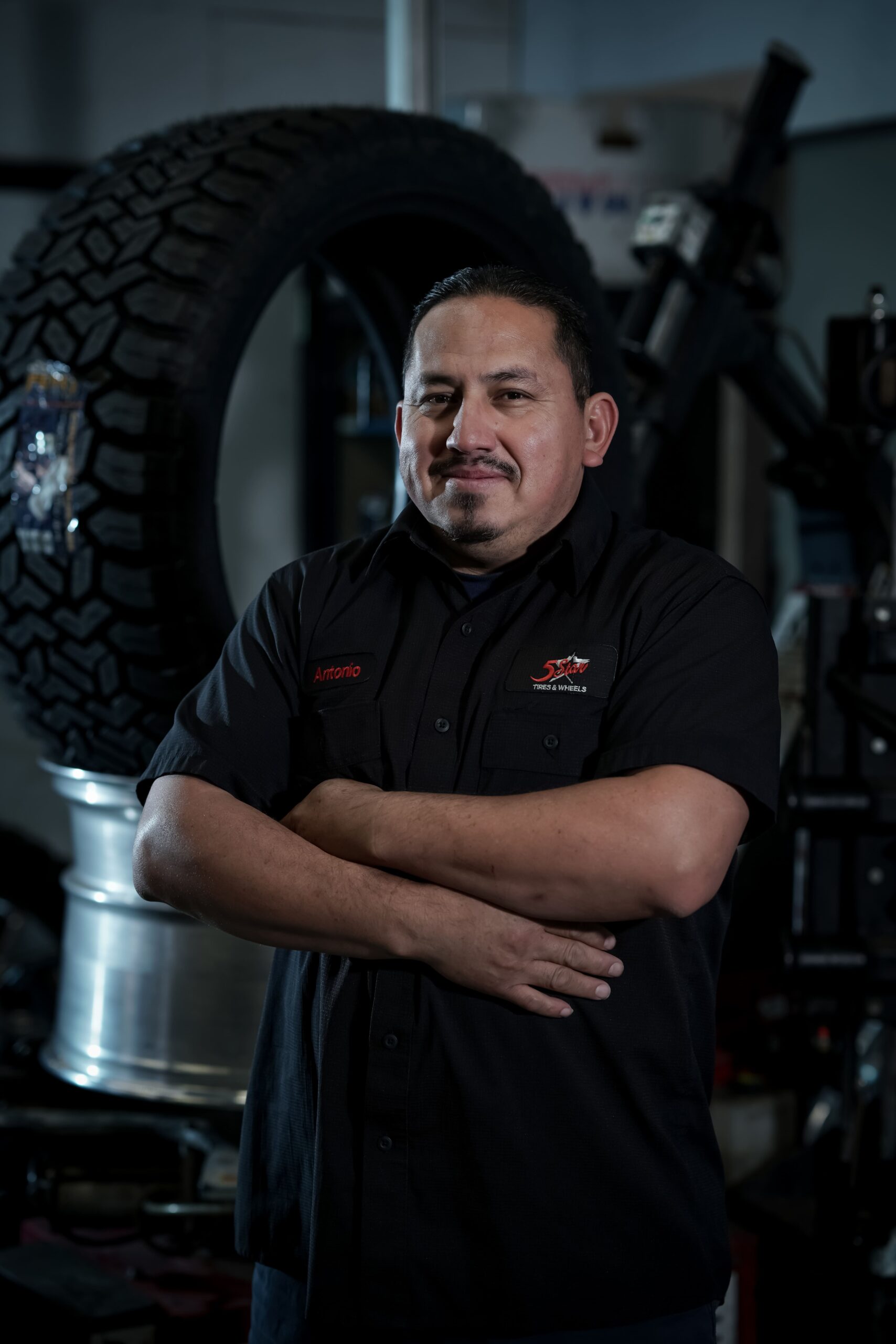 Skilled technician at 5 Star Tires and Wheels in front of large off-road tire.