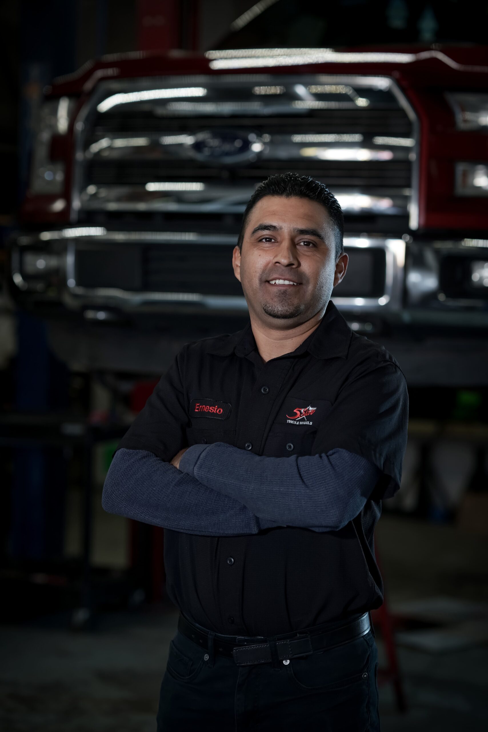 Friendly technician at 5 Star Tires and Wheels with a truck in the background.