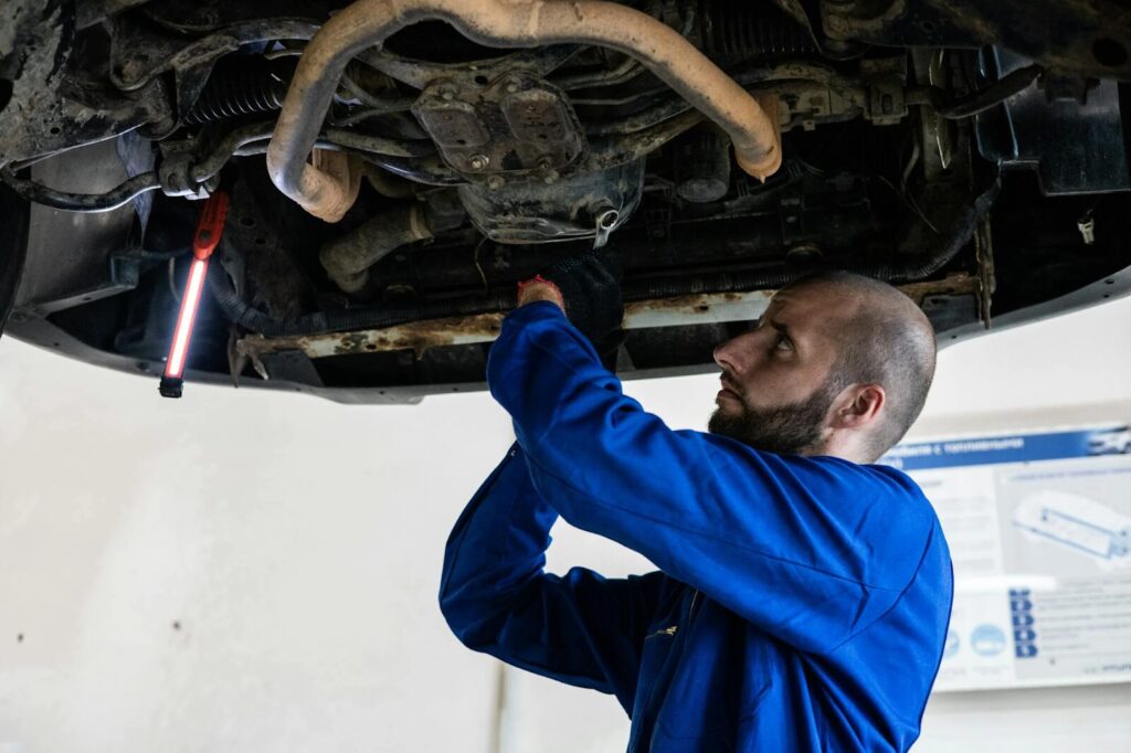 Auto mechanic inspecting car underside for repairs and maintenance.