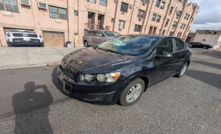 Used black sedan parked on street near apartment building.