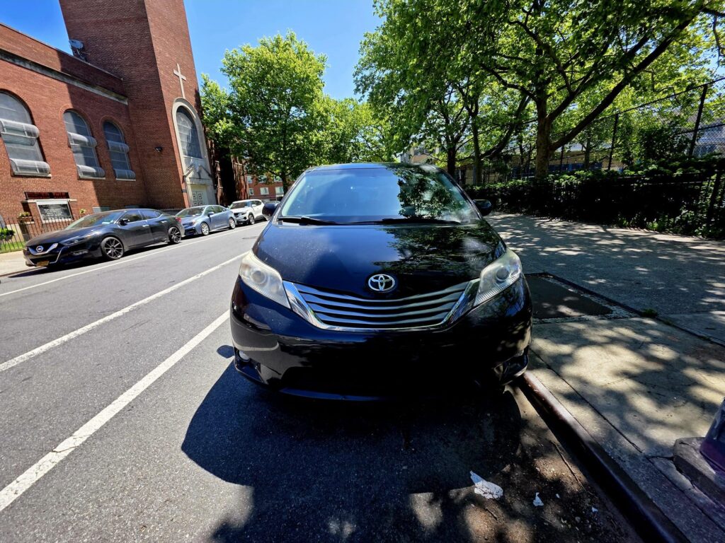 Toyota Prius parked on city street near church and trees.