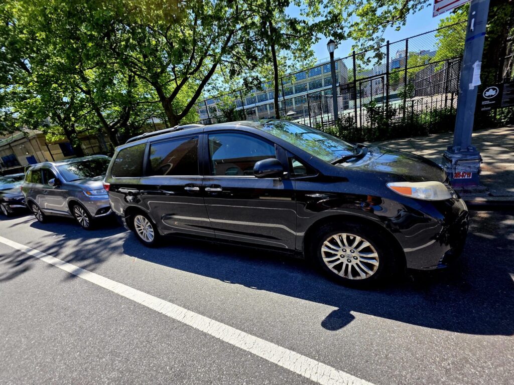 Black minivan parked along the curb in a sunny urban setting.