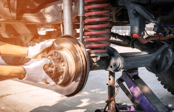 Auto repair technician inspecting vehicle suspension and brake system.