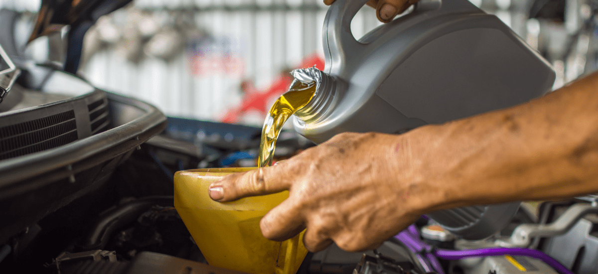 Mechanic pouring fresh motor oil into a car engine during oil change service.