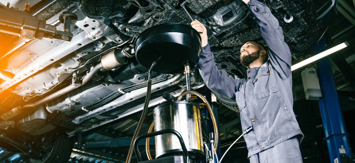 Auto mechanic performing oil change under vehicle.