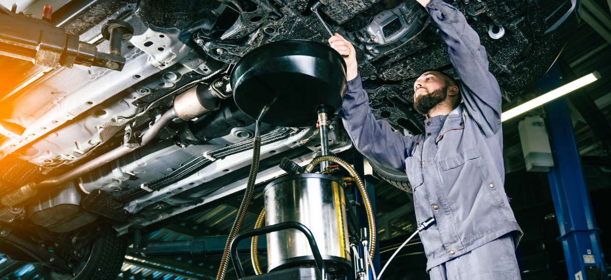 Auto mechanic inspecting vehicle's undercarriage for oil quality and engine health.