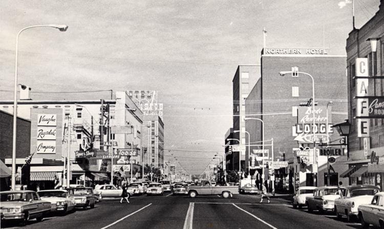 Historic downtown street scene with shops, cars, and signage.