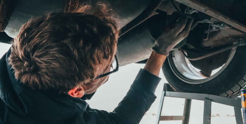 Skilled mechanic inspecting vehicle transmission undercarriage for repairs at AA Transmission.
