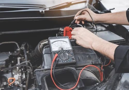 Technician testing car transmission with multimeter and diagnostic tools.