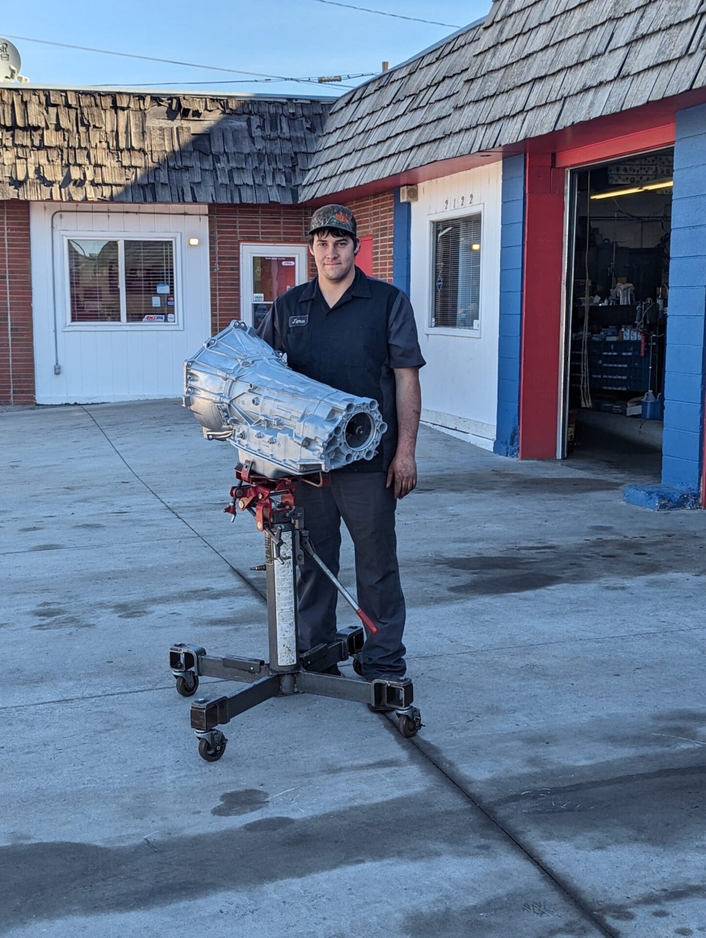 Transmission repair technician holding a transmission unit outside AA Transmission shop.