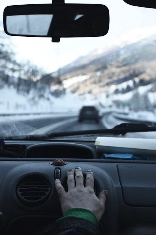 Inside view of a car dashboard with a hand on the gear shift during winter driving.
