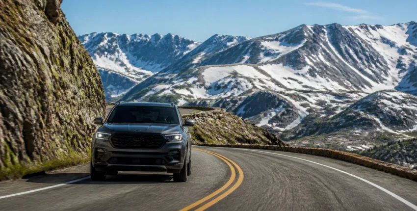 Black SUV driving on mountain road with snow-capped peaks in background.