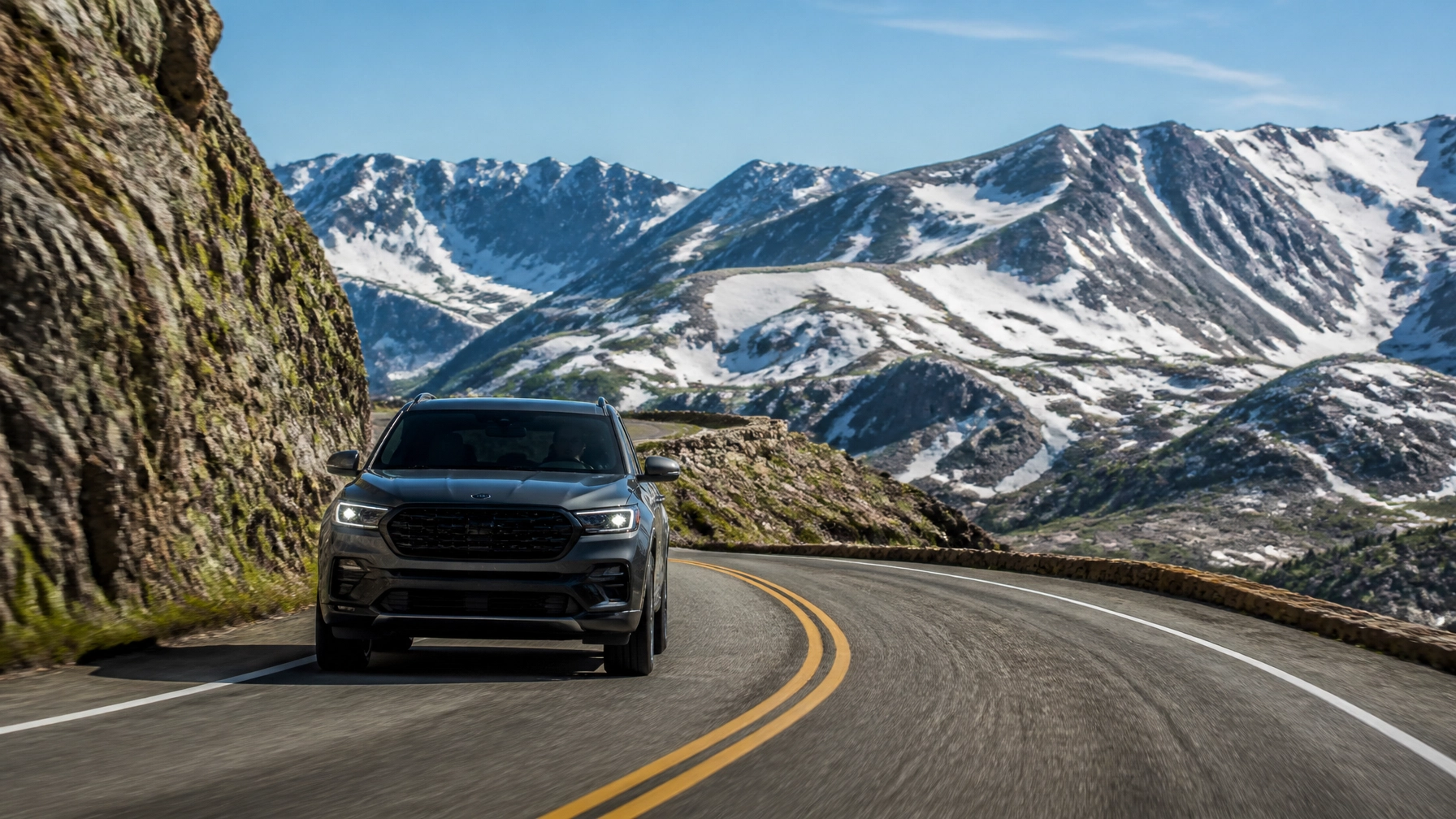 Black SUV driving on mountain road with snow-capped peaks in background.