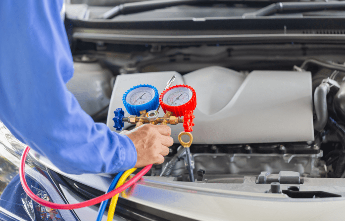 Technician checking car's air conditioning system with manifold gauge set.