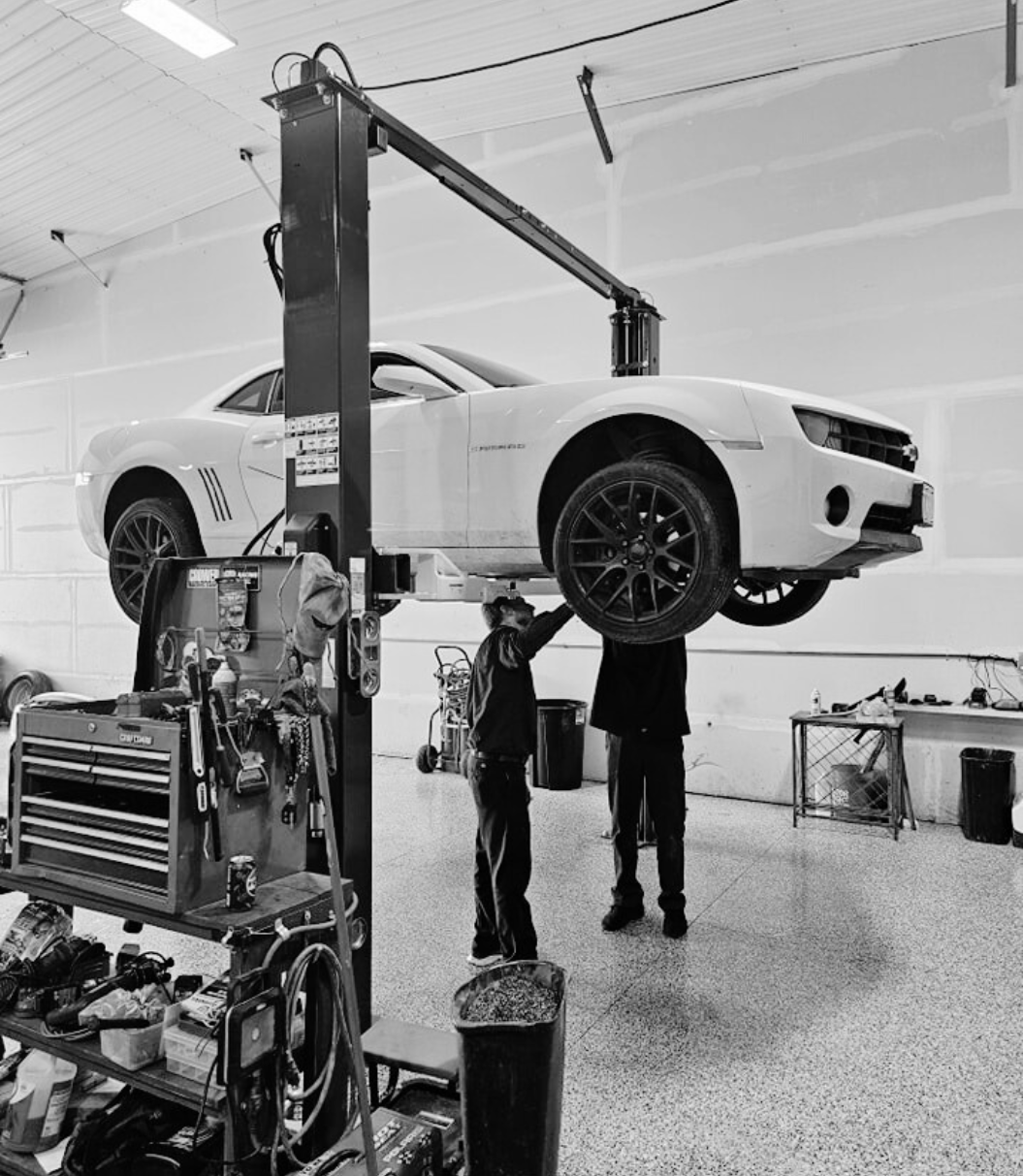 Auto repair technician inspecting a classic car on a hydraulic lift.
